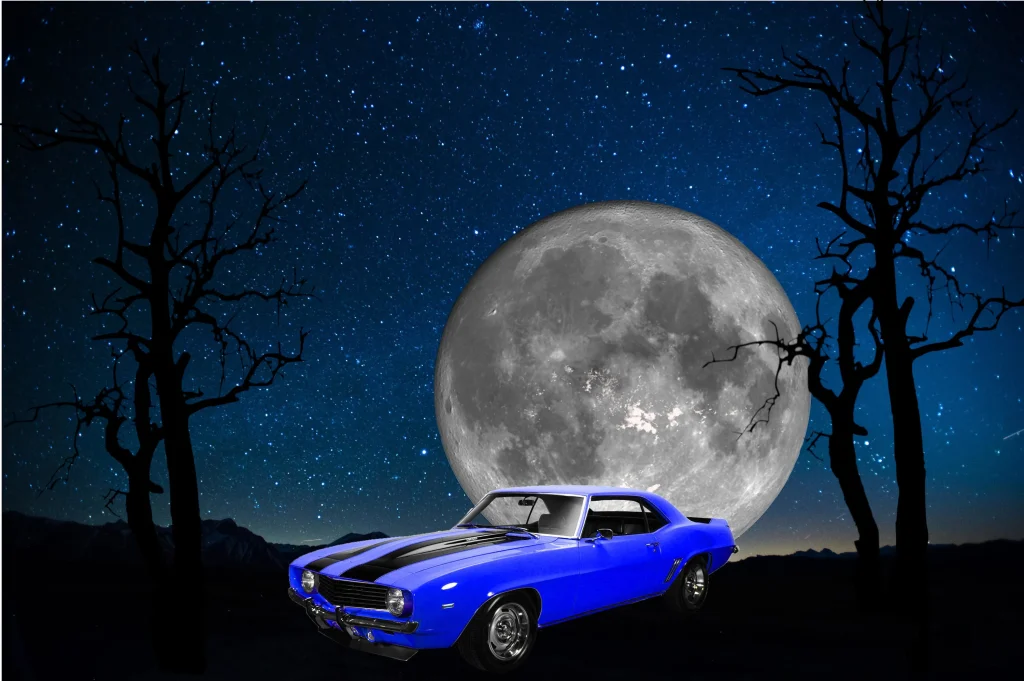 Blue 1969 Chevrolet Camaro Z28 under a full moon and starry sky.