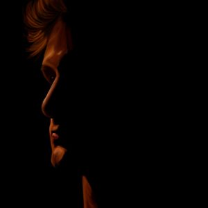 Portrait of a man in profile lit in warm red-orange tones against black.